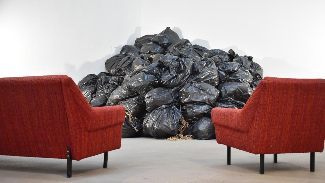 ein rotes Sofa und ein roter Sessel sind auf einen Berg aus schwarzen Mülltüten ausgerichtet. In der Ausstellung liefen dazu Geschichten von Frauen vom Tonband. 